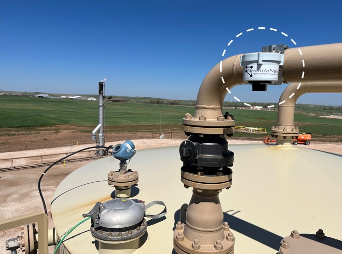 An endpoint installed above a thief hatch on a tank, with a vast green field in the background. The endpoint device is positioned atop the hatch, likely for methane monitoring or related purposes, against the backdrop of the expansive green landscape.